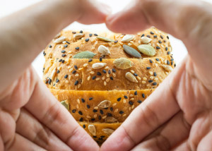 Hands forming heart shape in front of whole grain bread
