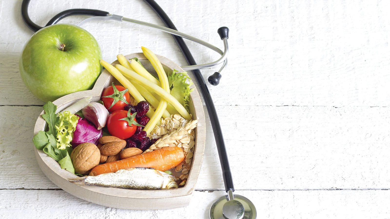 Nutritious fresh foods and seafood in a heart-shaped wood container surrounded by a stethiscope.