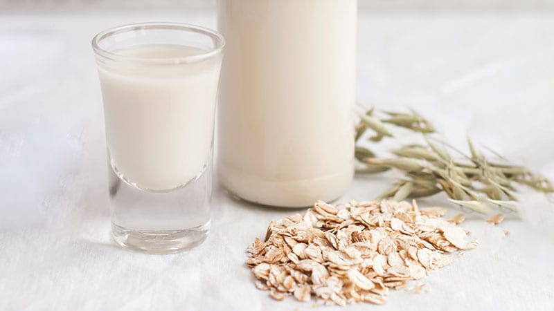 Oat milk in a glass next to a pile of loose oats.