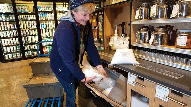 Makena Phillips, owner of Shepard Moon, pours Epsom salts into bulk bins from reusable plastic bags