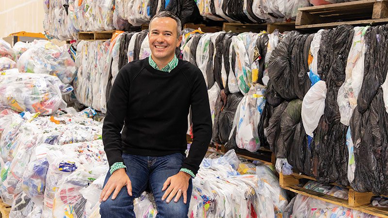 Ridwell CEO Ryan Metzger sitting on recycled bales of multi-layer plastics.